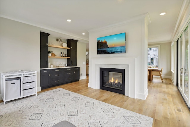 living room featuring a glass covered fireplace, light wood-type flooring, ornamental molding, and recessed lighting