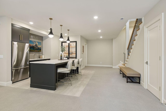 kitchen featuring recessed lighting, stainless steel refrigerator, light countertops, light colored carpet, and a center island