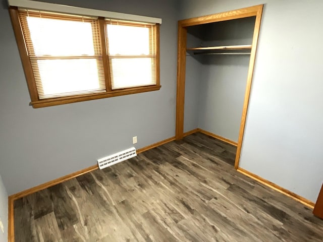 unfurnished bedroom featuring wood finished floors, visible vents, a closet, and baseboards