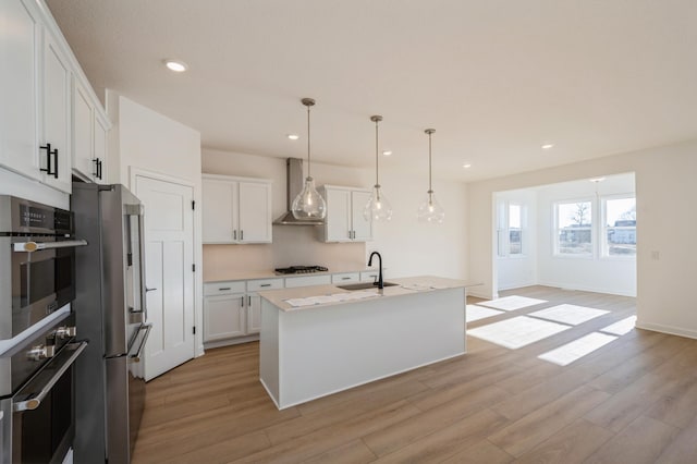 kitchen with white cabinetry, wall chimney range hood, light wood-style floors, and appliances with stainless steel finishes