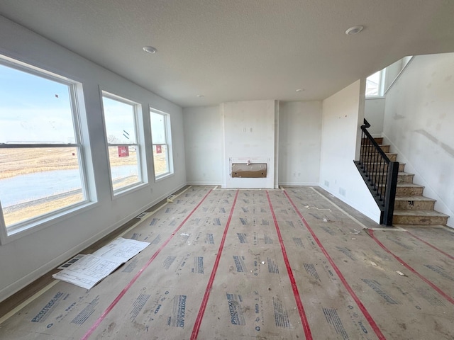 unfurnished living room with a wealth of natural light, stairway, and baseboards