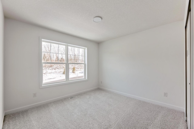 carpeted spare room featuring visible vents, a textured ceiling, and baseboards