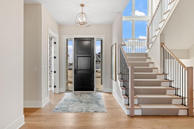 entrance foyer with stairway, baseboards, an inviting chandelier, and wood finished floors