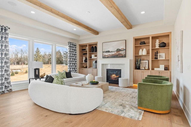 living room featuring beamed ceiling, built in shelves, a glass covered fireplace, wood finished floors, and recessed lighting