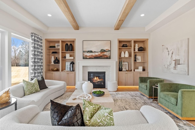 living room featuring a glass covered fireplace, beamed ceiling, built in features, and wood finished floors