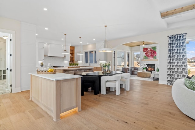 kitchen with open floor plan, a fireplace, light wood-style floors, custom exhaust hood, and open shelves