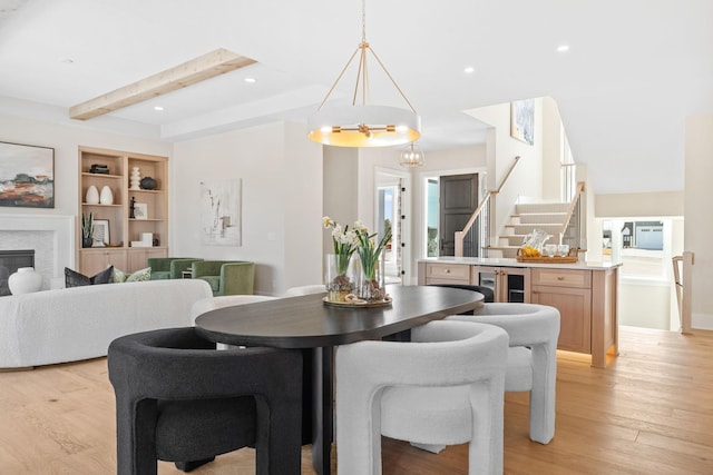 dining space featuring light wood finished floors, built in shelves, stairway, beam ceiling, and a glass covered fireplace