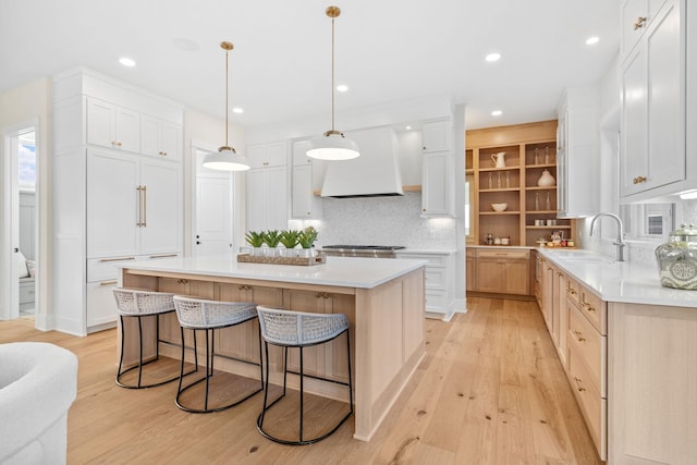 kitchen with custom exhaust hood, light countertops, light wood-style floors, and a sink