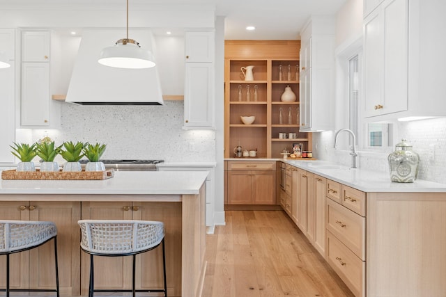 kitchen featuring light wood-style flooring, a sink, a kitchen breakfast bar, wall chimney exhaust hood, and light countertops