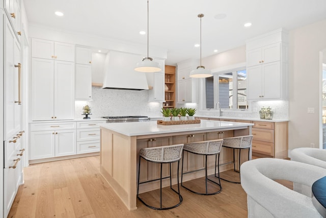 kitchen with a kitchen bar, premium range hood, white cabinetry, and light wood-type flooring