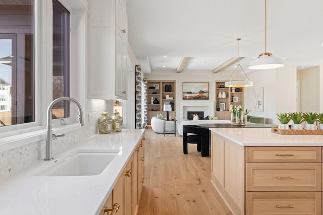 kitchen with light wood-type flooring, light brown cabinetry, a sink, a warm lit fireplace, and light countertops