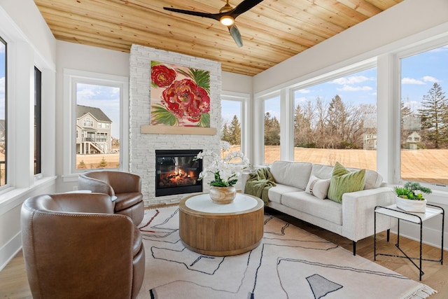 sunroom with a stone fireplace, wood ceiling, and ceiling fan