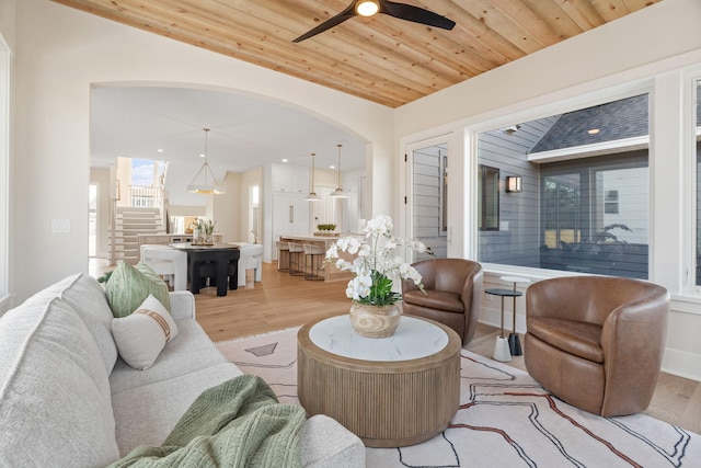 living room featuring stairway, a ceiling fan, arched walkways, wood ceiling, and light wood-type flooring