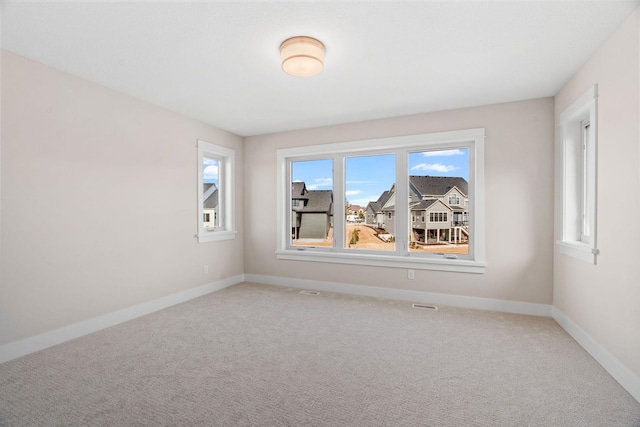 spare room with a wealth of natural light, visible vents, baseboards, and light carpet