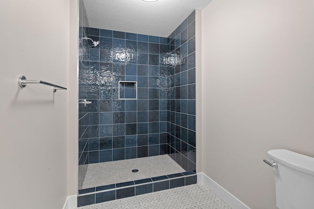 bathroom featuring a tile shower, a textured ceiling, toilet, and baseboards