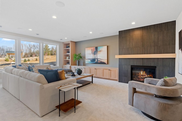 living area featuring a glass covered fireplace, recessed lighting, light colored carpet, and built in features