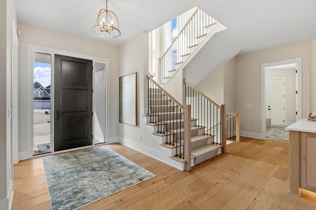 entrance foyer with light wood-style flooring, stairway, baseboards, and a chandelier