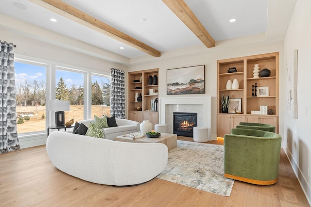 living area with a glass covered fireplace, beam ceiling, wood finished floors, built in shelves, and recessed lighting