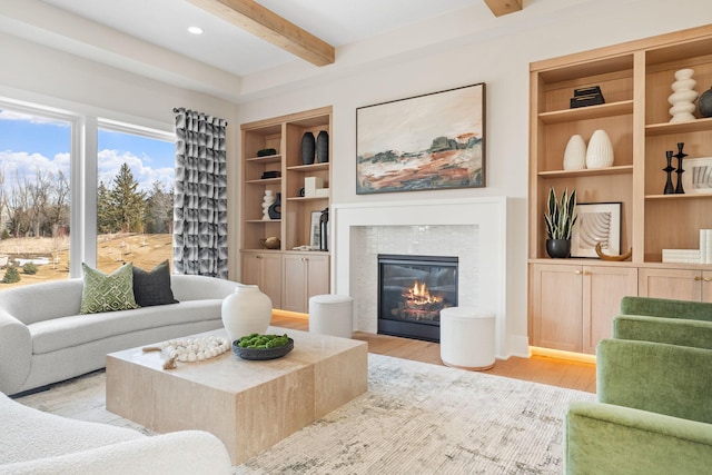 living area with beam ceiling, light wood-type flooring, a tiled fireplace, and built in shelves