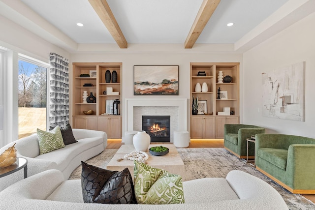 living area featuring wood finished floors, beamed ceiling, a glass covered fireplace, built in features, and recessed lighting