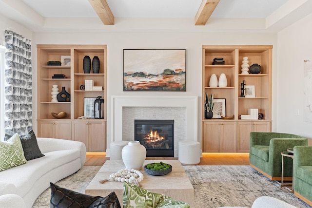 living area with beamed ceiling, wood finished floors, a glass covered fireplace, and built in shelves