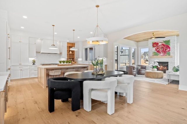 dining space with light wood-style flooring, a glass covered fireplace, arched walkways, recessed lighting, and a ceiling fan