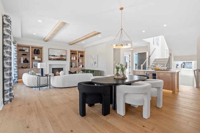 dining room featuring light wood-style flooring, beamed ceiling, stairway, a glass covered fireplace, and a chandelier