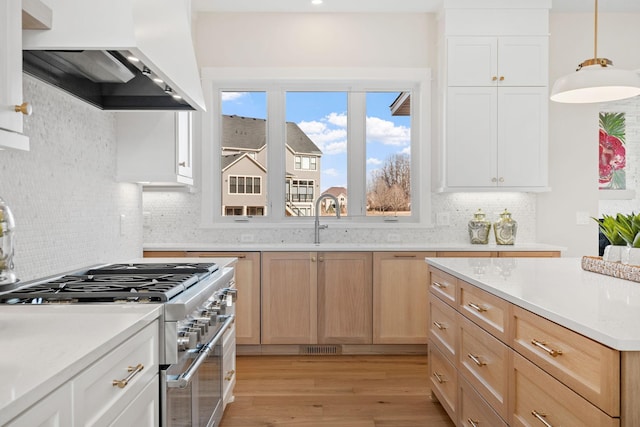 kitchen with wall chimney range hood, high end stainless steel range, decorative backsplash, light wood-type flooring, and a sink