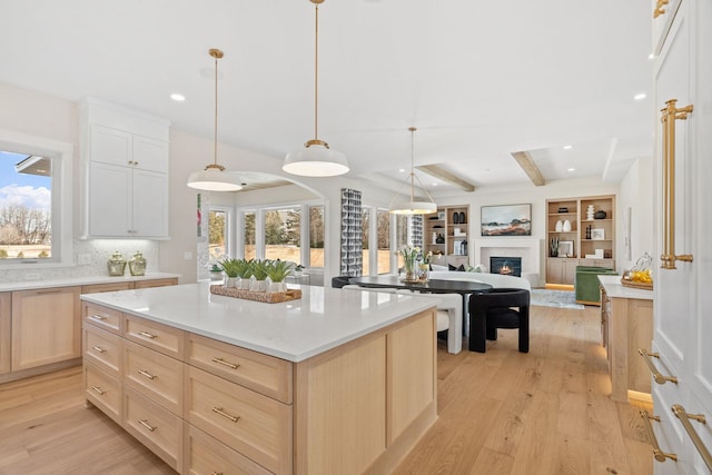 kitchen featuring light brown cabinetry, open floor plan, light wood finished floors, light countertops, and beamed ceiling
