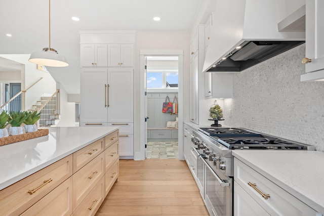 kitchen with premium range hood, high end stove, light wood-style floors, backsplash, and pendant lighting
