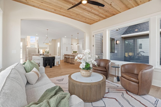 living room featuring light wood-style floors, wood ceiling, ceiling fan, stairway, and arched walkways
