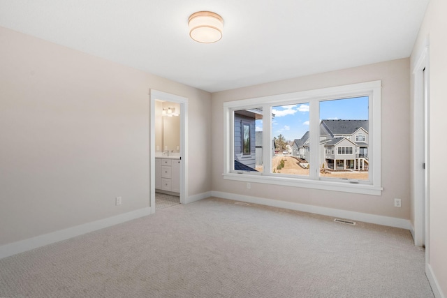unfurnished bedroom featuring light carpet, baseboards, and ensuite bathroom