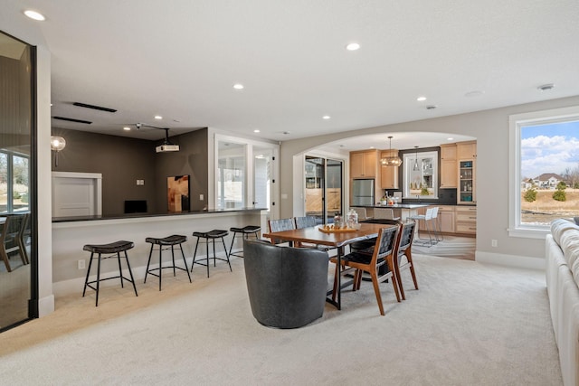 dining room featuring light carpet, arched walkways, recessed lighting, plenty of natural light, and baseboards