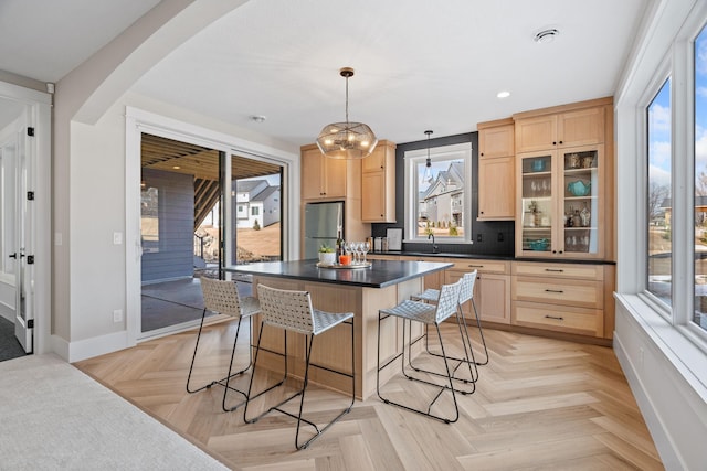 kitchen featuring light brown cabinetry, freestanding refrigerator, a breakfast bar area, dark countertops, and baseboards
