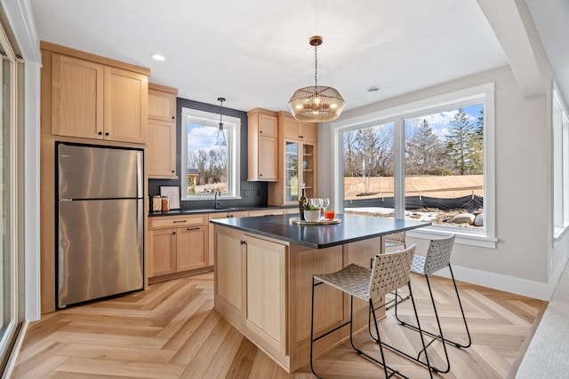 kitchen featuring freestanding refrigerator, light brown cabinetry, dark countertops, baseboards, and a chandelier
