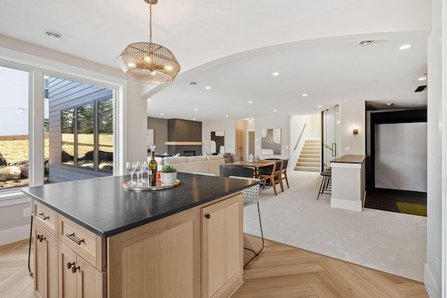 kitchen with dark countertops, light brown cabinets, a kitchen island, open floor plan, and pendant lighting
