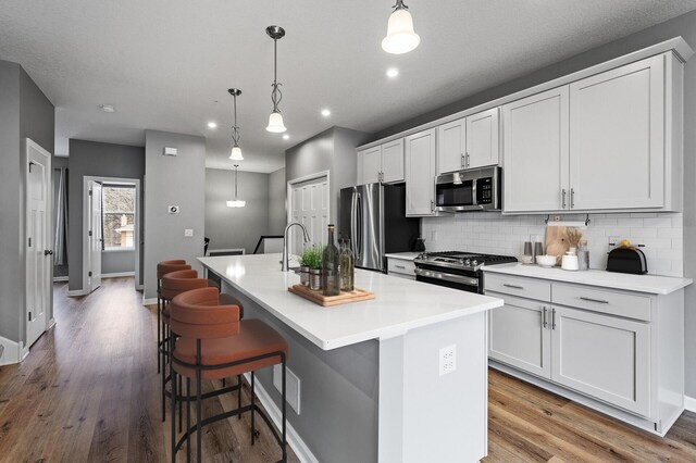 kitchen featuring backsplash, baseboards, appliances with stainless steel finishes, and a kitchen island with sink