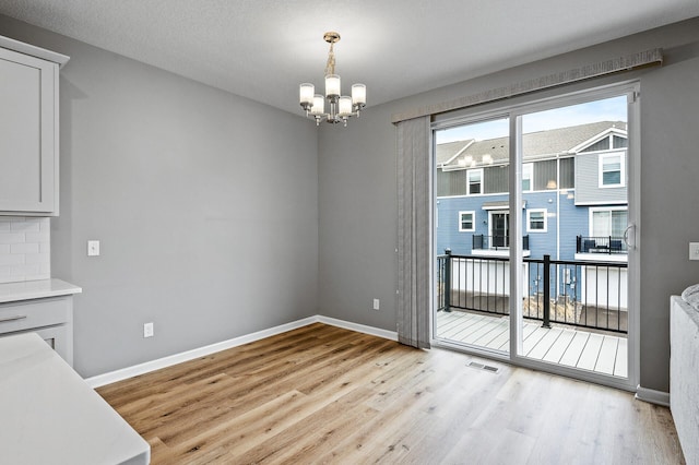 unfurnished dining area featuring visible vents, light wood finished floors, baseboards, and a notable chandelier