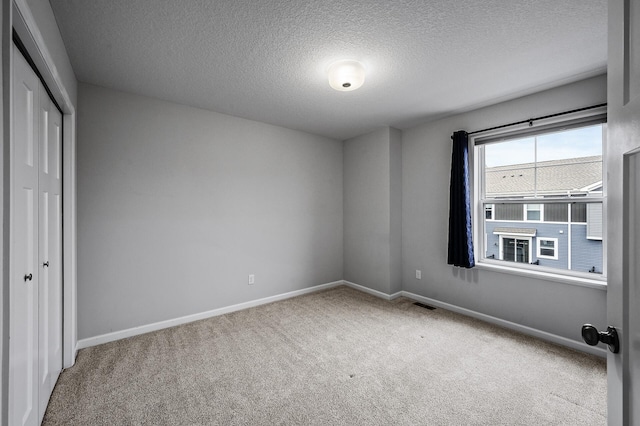 unfurnished bedroom featuring a textured ceiling, a closet, baseboards, carpet flooring, and visible vents
