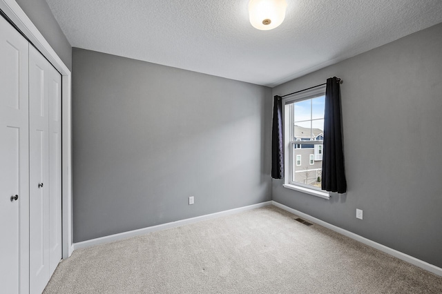 unfurnished bedroom featuring a closet, a textured ceiling, carpet flooring, and visible vents