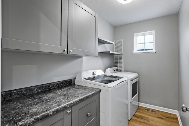 clothes washing area featuring visible vents, washing machine and dryer, light wood-style floors, baseboards, and cabinet space