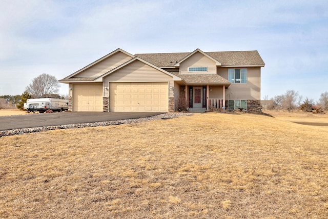 traditional-style home featuring a front yard, roof with shingles, a garage, stone siding, and aphalt driveway