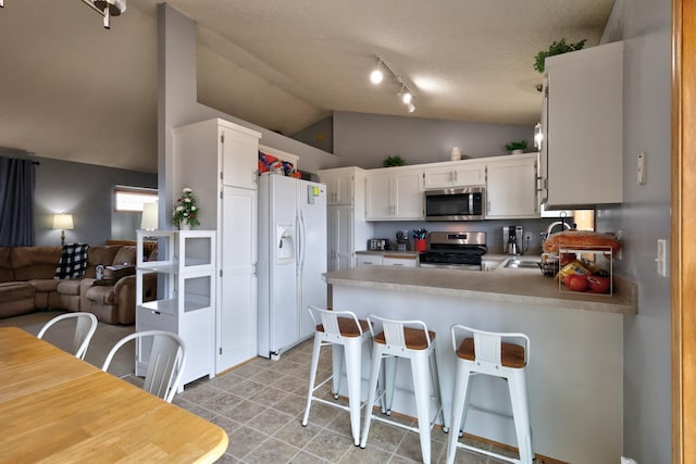 kitchen with open floor plan, a peninsula, white cabinets, stainless steel appliances, and a sink