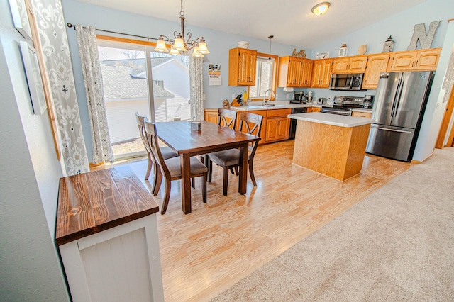 kitchen with a sink, light countertops, vaulted ceiling, appliances with stainless steel finishes, and light wood-type flooring