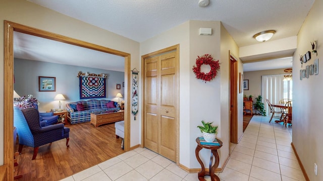 hall with baseboards, a textured ceiling, and light tile patterned flooring