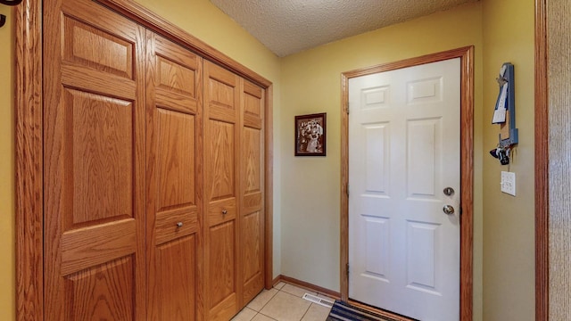 doorway featuring light tile patterned floors, visible vents, baseboards, and a textured ceiling