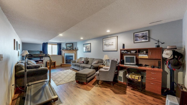 living room featuring a glass covered fireplace, recessed lighting, wood finished floors, and a textured ceiling