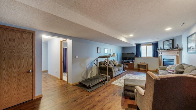 living area featuring visible vents, a textured ceiling, a glass covered fireplace, wood-type flooring, and baseboards