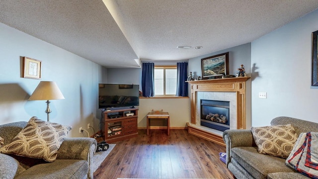 living area with a tile fireplace, a textured ceiling, baseboards, and wood finished floors