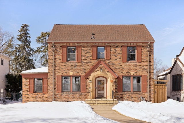 view of front facade with brick siding, a shingled roof, and fence